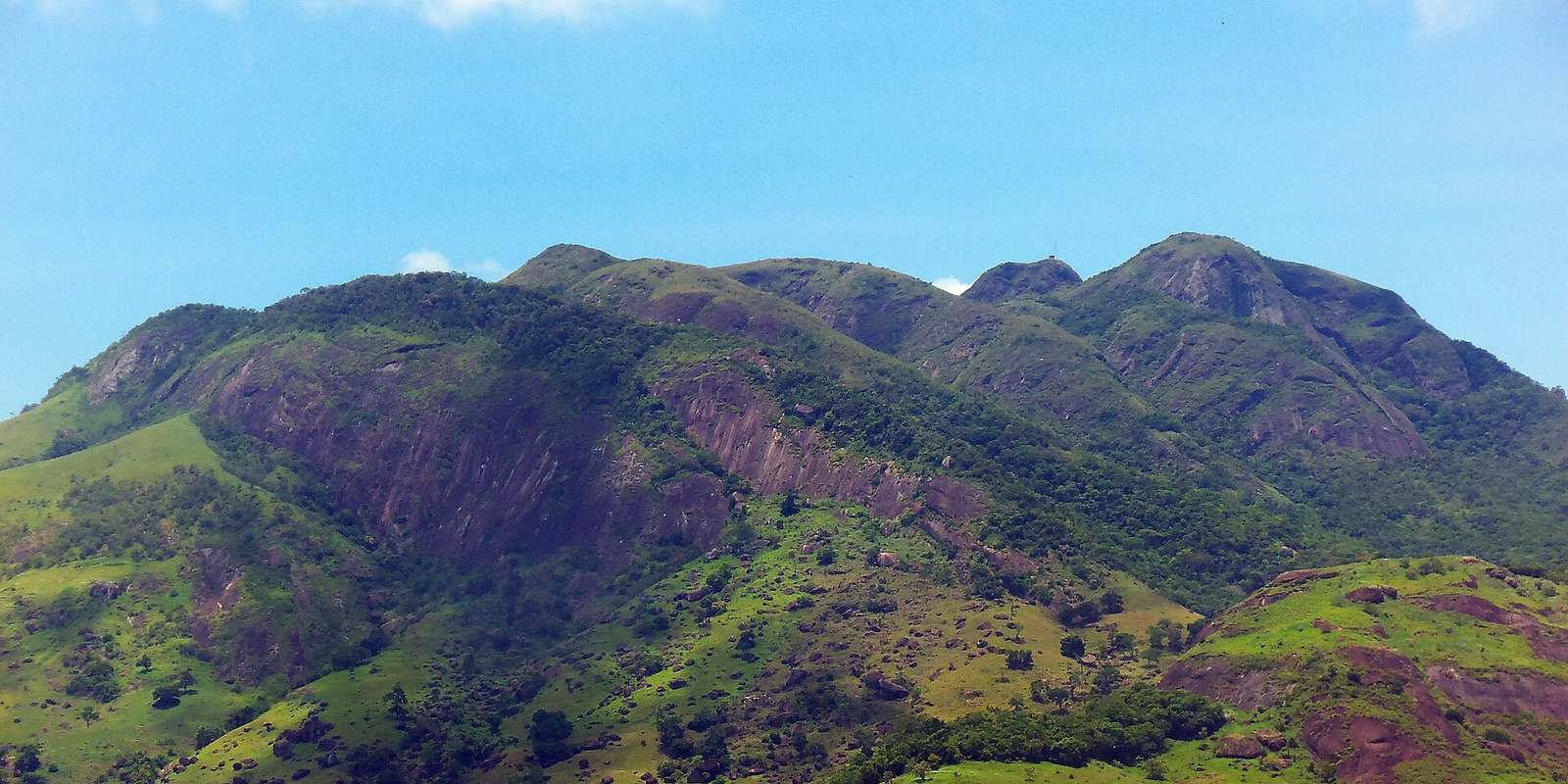 Maciço do Mestre Álvaro, coberto de mata e pasto, sob céu azul na Serra